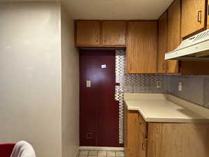 Kitchen featuring light tile patterned flooring, backsplash, and extractor fan