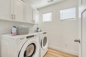 Washroom with washer and clothes dryer, cabinets, and light wood-type flooring