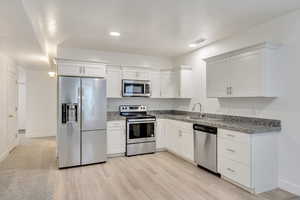 Kitchen with white cabinets, light wood-type flooring, stainless steel appliances, and sink