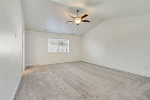 Carpeted spare room with ceiling fan and vaulted ceiling