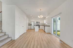 Kitchen featuring white cabinets, hanging light fixtures, light hardwood / wood-style flooring, appliances with stainless steel finishes, and a kitchen island