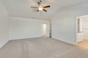 Interior space featuring ensuite bathroom, ceiling fan, light carpet, and lofted ceiling