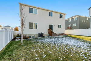 Snow covered back of property with a lawn and central AC