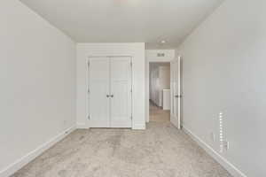 Unfurnished bedroom featuring light carpet and a closet