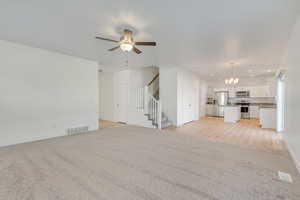 Unfurnished living room featuring light carpet, ceiling fan with notable chandelier, and sink