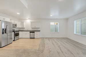 Kitchen with white cabinetry, sink, light wood-type flooring, and appliances with stainless steel finishes