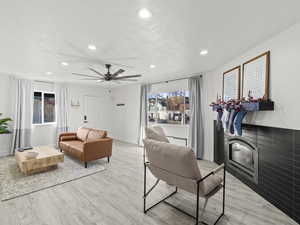 Living room with a fireplace, light hardwood / wood-style floors, and ceiling fan