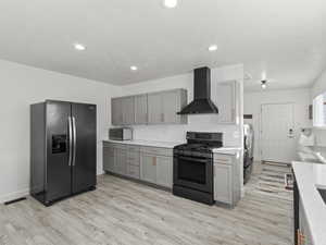 Kitchen featuring gray cabinets, light hardwood / wood-style flooring, stainless steel appliances, and wall chimney range hood