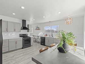 Kitchen featuring gas stove, wall chimney range hood, decorative light fixtures, light hardwood / wood-style flooring, and black dishwasher