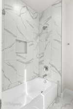 Full bathroom featuring shower / bath combination, marble look tiles, and baseboards