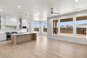 Kitchen featuring stainless steel appliances, light countertops, an island with sink, a ceiling fan, and a sink