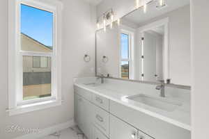 Bathroom with marble look tiles, healthy amount of natural light, baseboards, and double vanity