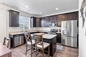 Kitchen featuring a center island, light hardwood / wood-style flooring, appliances with stainless steel finishes, dark brown cabinets, and a kitchen bar