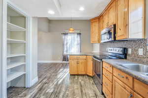 Kitchen with appliances with stainless steel finishes, tasteful backsplash, pendant lighting, and hardwood / wood-style floors