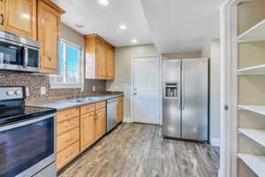 Kitchen featuring decorative backsplash, sink, light hardwood / wood-style floors, and appliances with stainless steel finishes