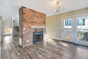 Unfurnished living room featuring a notable chandelier, dark hardwood / wood-style floors, and a brick fireplace