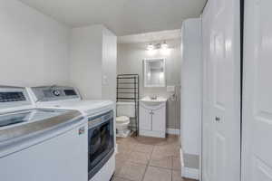 Laundry area with washer and clothes dryer, an inviting chandelier, sink, a textured ceiling, and light tile patterned flooring