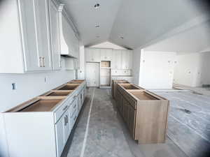 Kitchen featuring concrete flooring, lofted ceiling, a kitchen island, and white cabinets