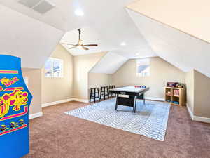 Rec room featuring carpet floors, vaulted ceiling, ceiling fan, and a healthy amount of sunlight