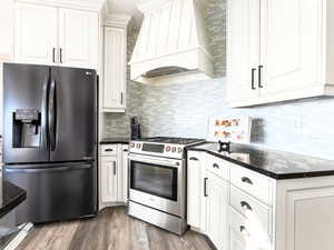 Kitchen with premium range hood, dark hardwood / wood-style floors, dark stone countertops, white cabinetry, and stainless steel appliances