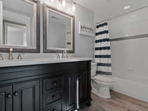 Full bathroom with hardwood / wood-style floors, vanity, toilet, and shower / tub combo with curtain