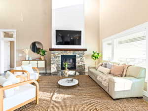 Living room with a stone fireplace, wood-type flooring, and high vaulted ceiling