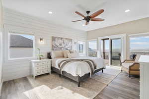 Bedroom featuring access to exterior, light wood-type flooring, ceiling fan, and wood walls