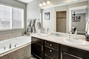 Bathroom featuring tiled tub, ceiling fan, and vanity