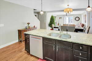 Kitchen featuring dishwasher, sink, hanging light fixtures, light hardwood / wood-style flooring, and ornate columns