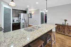 Kitchen featuring wood-type flooring, stainless steel refrigerator with ice dispenser, light stone counters, and sink