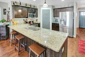 Kitchen with sink, stainless steel appliances, kitchen peninsula, wood-type flooring, and decorative light fixtures