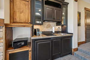 Kitchen featuring decorative backsplash, black electric stovetop, light stone counters, and sink