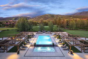 Pool at dusk featuring a mountain view, an in ground hot tub, and a patio