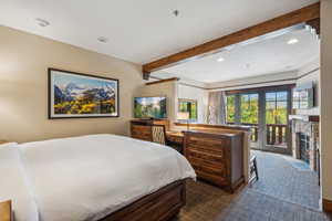 Bedroom with beamed ceiling, dark carpet, access to outside, and a stone fireplace