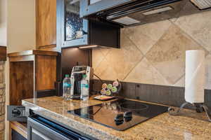 Kitchen with decorative backsplash, black electric stovetop, light stone counters, and extractor fan