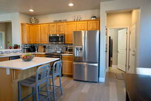 Kitchen featuring backsplash, a center island, light wood-type flooring, and stainless steel appliances