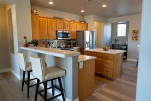 Kitchen featuring light wood-type flooring, appliances with stainless steel finishes, a kitchen island, kitchen peninsula, and a breakfast bar area