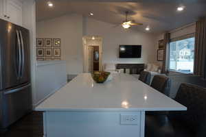 Kitchen with a kitchen bar, vaulted ceiling, stainless steel refrigerator, and a kitchen island