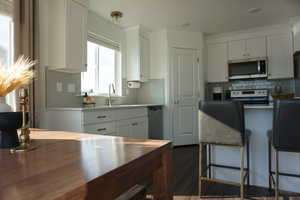 Kitchen with appliances with stainless steel finishes, backsplash, white cabinetry, and dark hardwood / wood-style flooring