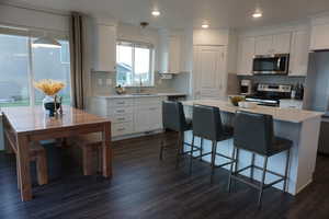 Kitchen featuring white cabinetry, sink, stainless steel appliances, dark hardwood / wood-style floors, and decorative light fixtures