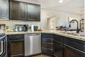 Kitchen featuring sink, appliances with stainless steel finishes, dark brown cabinets, light hardwood / wood-style floors, and light stone counters