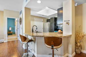 Kitchen featuring kitchen peninsula, dark hardwood / wood-style flooring, a breakfast bar, sink, and stainless steel refrigerator