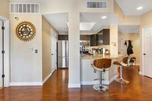 Kitchen with kitchen peninsula, appliances with stainless steel finishes, light stone countertops, a kitchen breakfast bar, and dark hardwood / wood-style floors