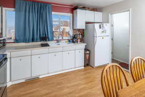 Kitchen featuring light wood-type flooring, sink, stainless steel stove, white cabinets, and white fridge