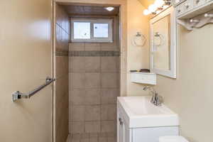 Bathroom with tile patterned flooring, vanity, tiled shower, and toilet