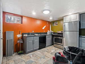 Kitchen featuring a textured ceiling, stainless steel appliances, gray cabinets, and sink