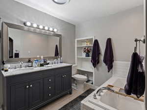 Bathroom with a textured ceiling, vanity, tiled bath, and toilet