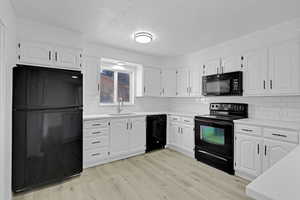 Kitchen featuring tasteful backsplash, sink, black appliances, light hardwood / wood-style flooring, and white cabinetry