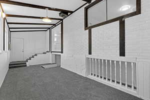 Carpeted empty room with vaulted ceiling with beams and brick wall