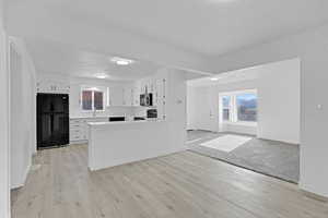 Kitchen featuring white cabinets, black appliances, a textured ceiling, and light hardwood / wood-style floors